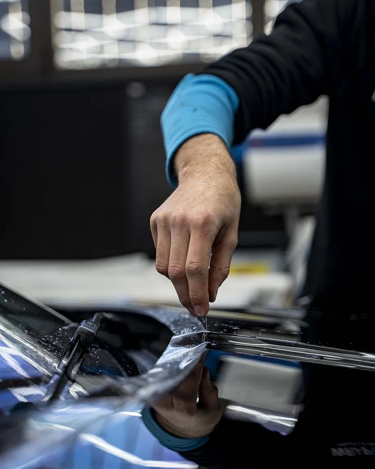 Mano di un applicatore che stende la pellicola sul cofano di un'auto da corsa